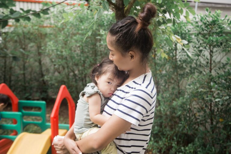 A woman holds a baby in an outdoor garden, conveying warmth and care.