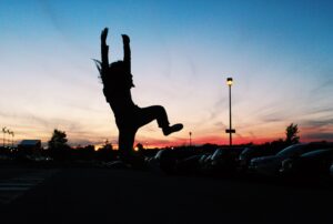 A dynamic silhouette scene of a person jumping joyously in a parking lot at sunset, capturing an energetic moment.