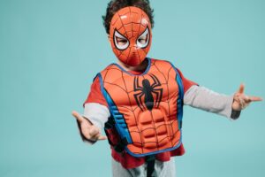 Child wearing a Spiderman costume and mask striking a playful superhero pose in a studio setting.