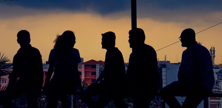 Silhouette of diverse group chatting against Bengaluru skyline at twilight.