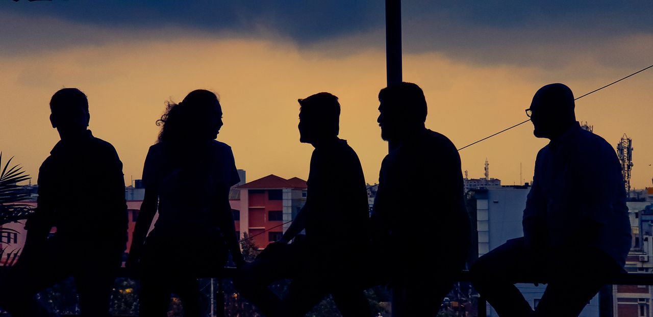Silhouette of diverse group chatting against Bengaluru skyline at twilight.