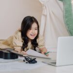 Adorable child engaging in online learning with a ukulele and laptop indoors.