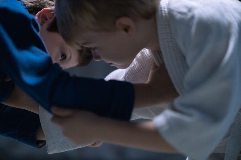 Two young boys engage in jiu jitsu training, focusing on combat skills indoors.